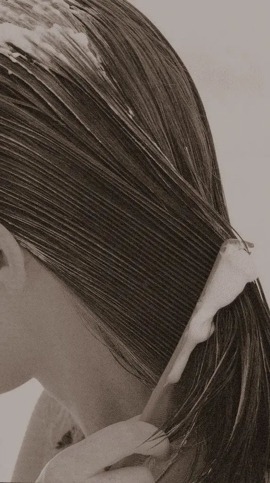 “Person applying conditioner to wet hair with a comb, spreading product evenly along the strands in a close-up haircare routine.”