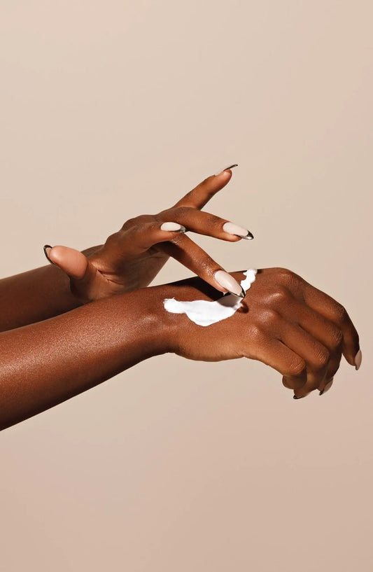 “Close-up of hands applying a white moisturizing cream on skin, gently massaging the product over the forearm against a neutral background.”