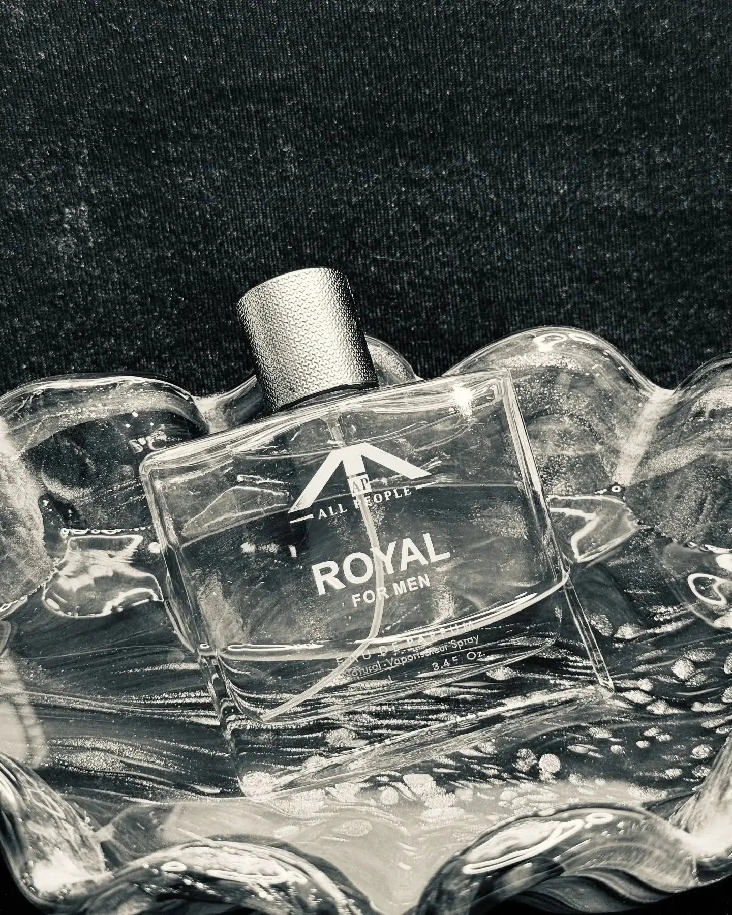“All People ‘Royal’ perfume for men, placed inside a sculpted glass dish with metallic reflections, photographed in a monochrome setting for a refined, premium look.”