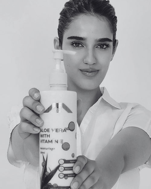Woman holding All People Aloe Vera with Vitamin E moisturizer bottle against a plain background